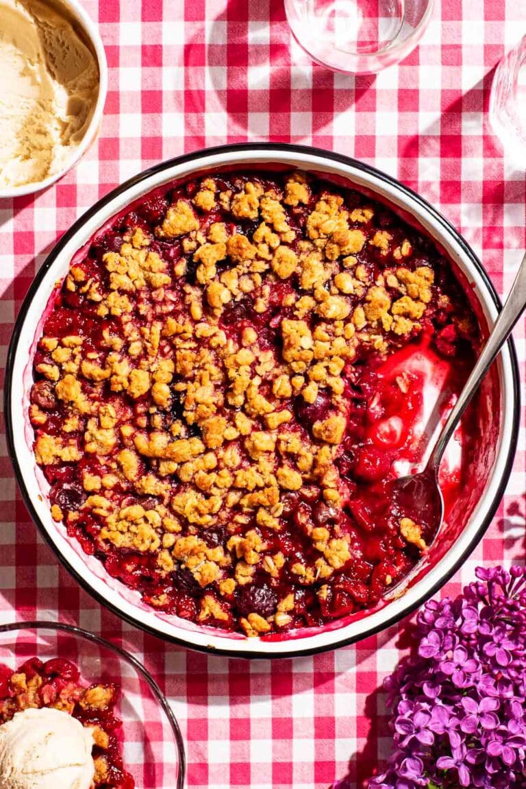 Cherry oat crisp on a red gingham tablecloth with vanilla ice cream and lilacs.