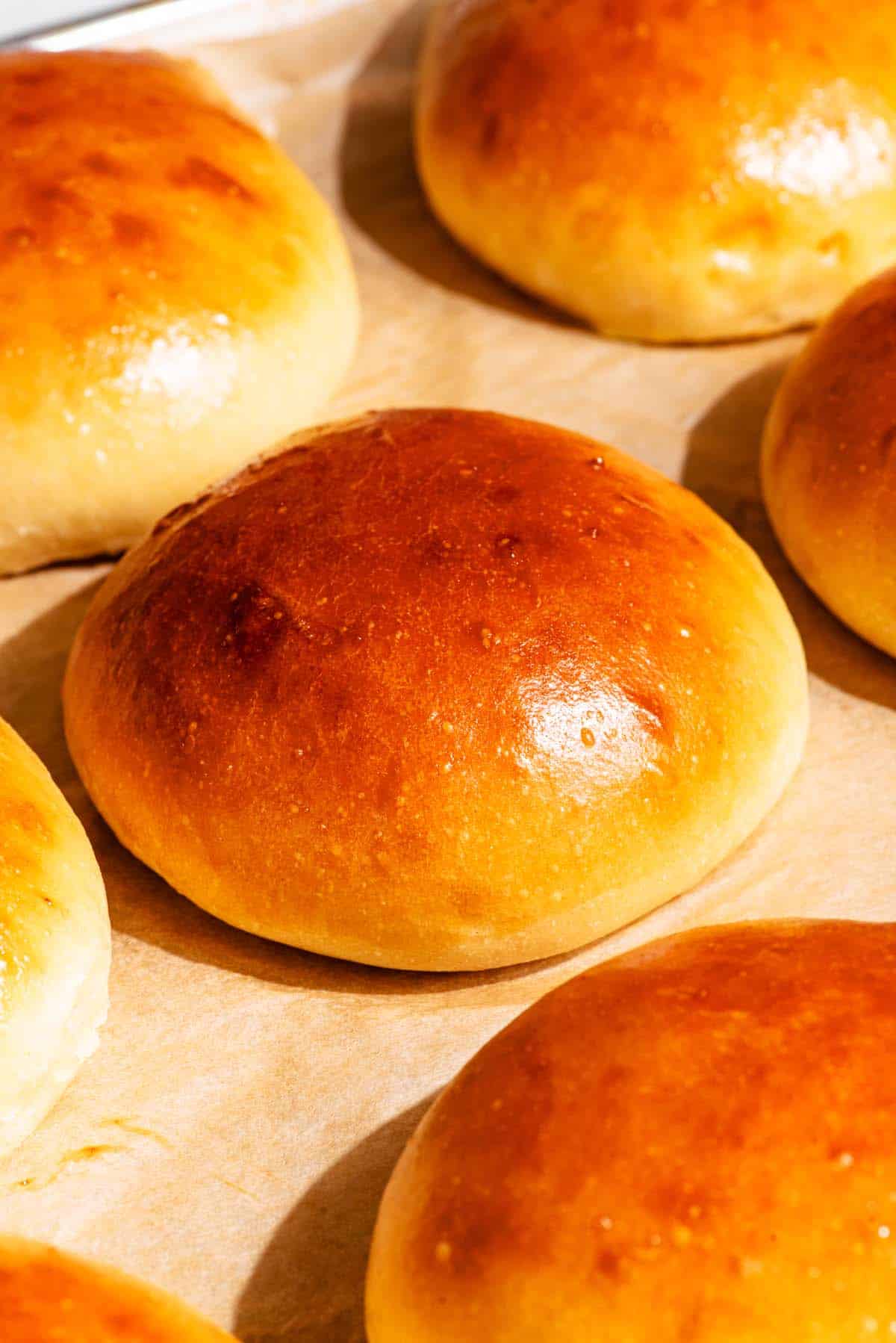 Several shiny burger buns on parchment paper.