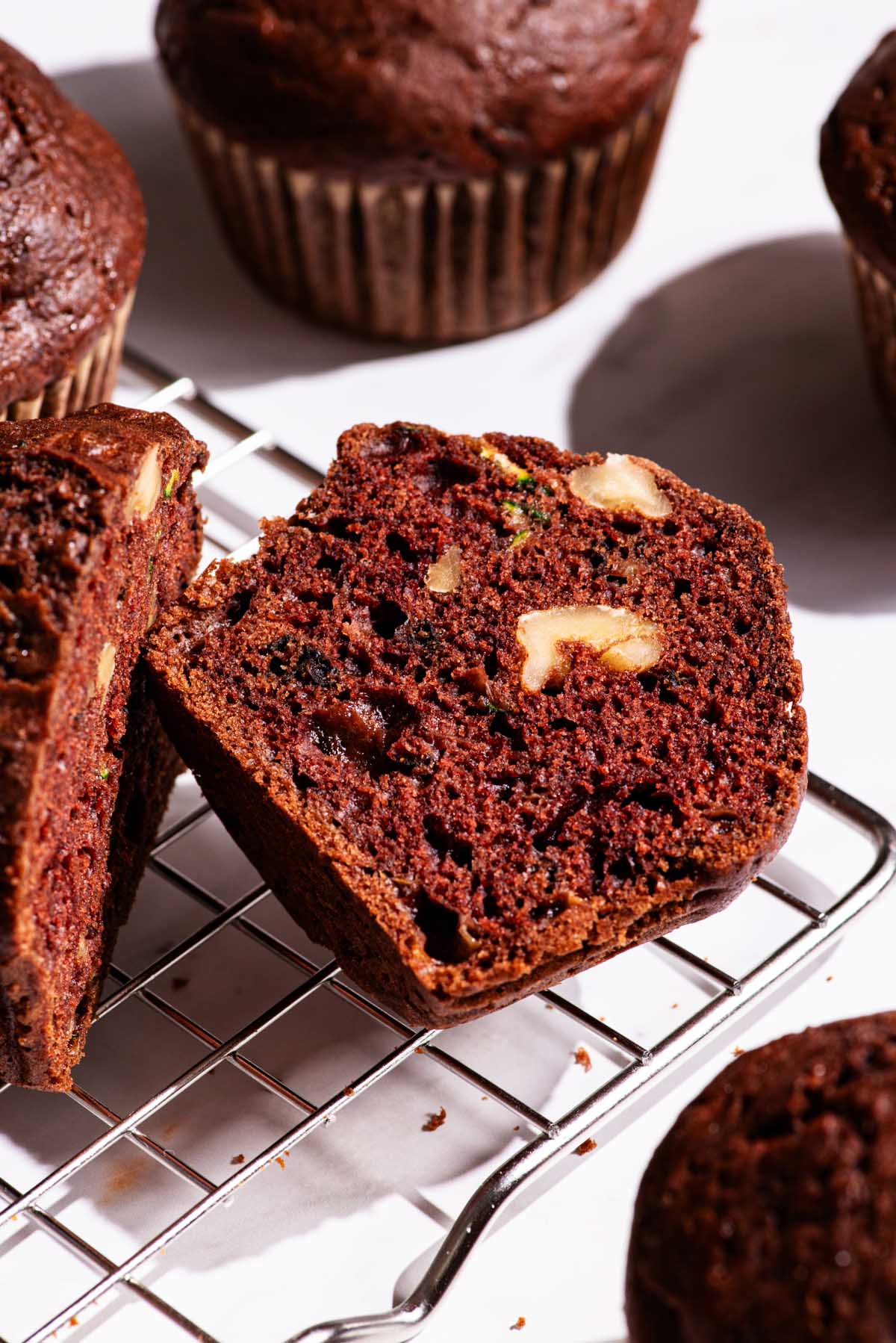 Chocolate muffins on a wire rack, one halved to show interior texture.