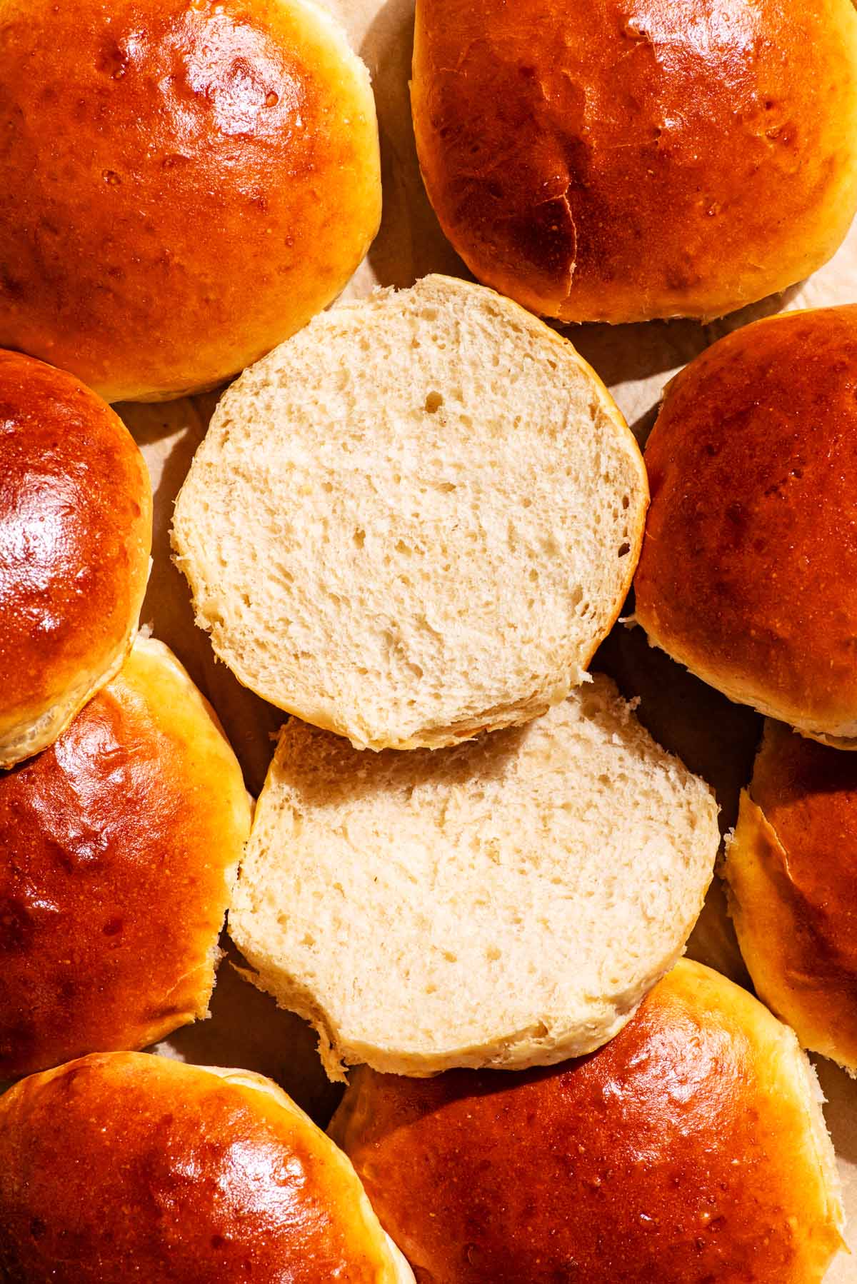 Several burger buns, one sliced and turned so both pieces are cut-side up to show the interior.