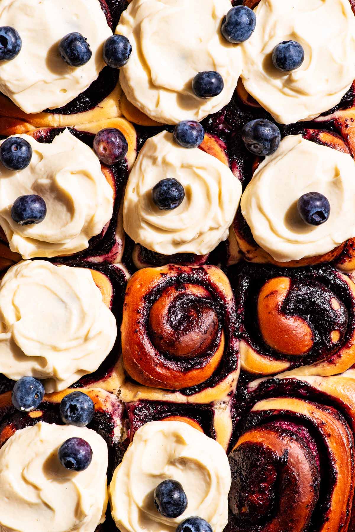 Top-down view of cinnamon rolls with blueberries and frosting.