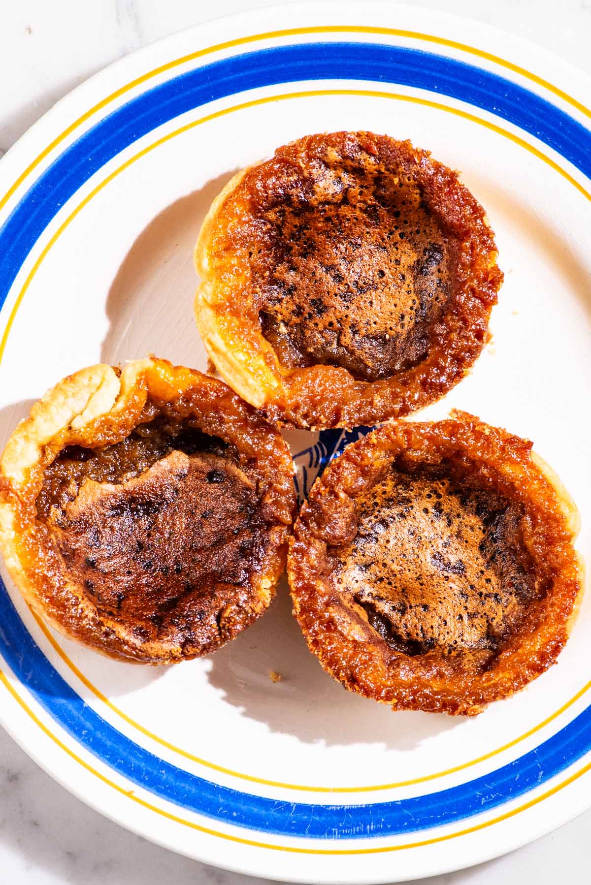 Three small butter tarts on a plate with a blue rim.