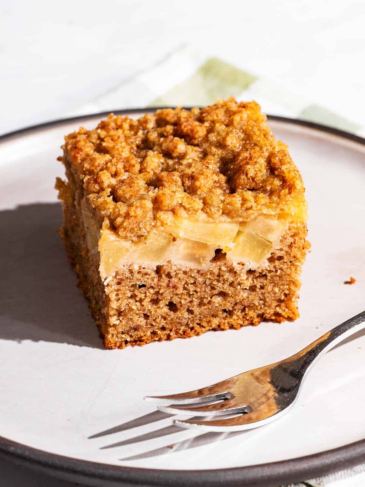 A small square of apple crumb cake on a plate with a cake fork.