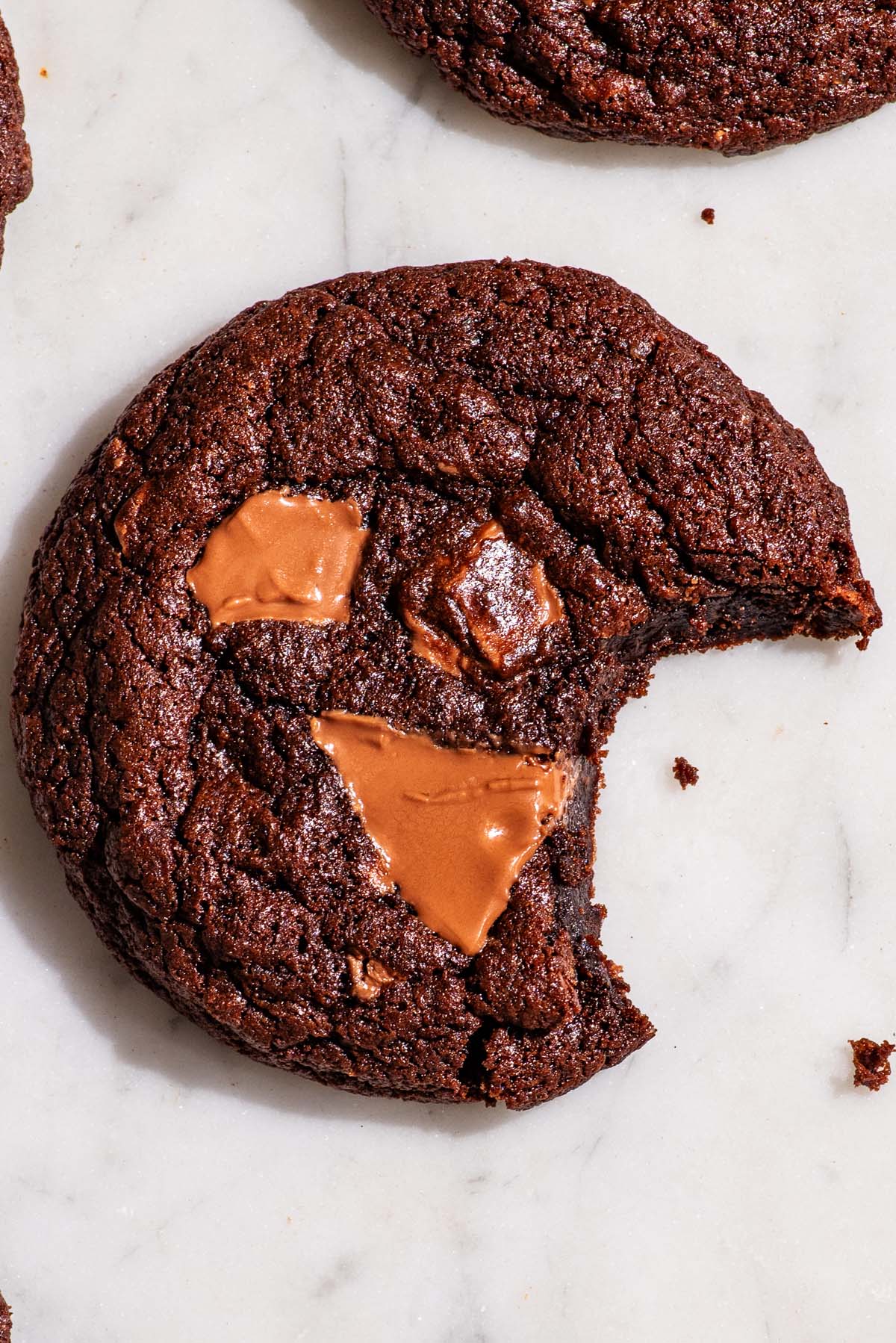 Double chocolate cookies on a marble board, with a bite taken out of the cookie.