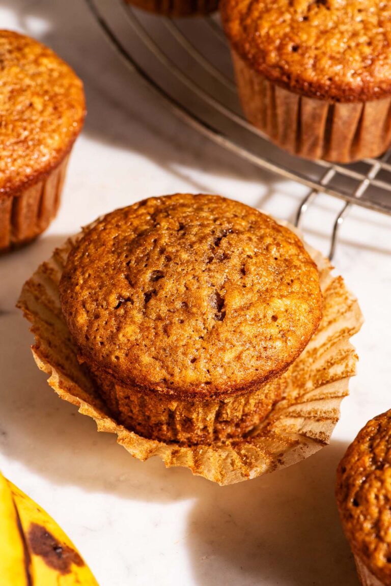 Four muffins on a marble counter, one with the paper lining removed.