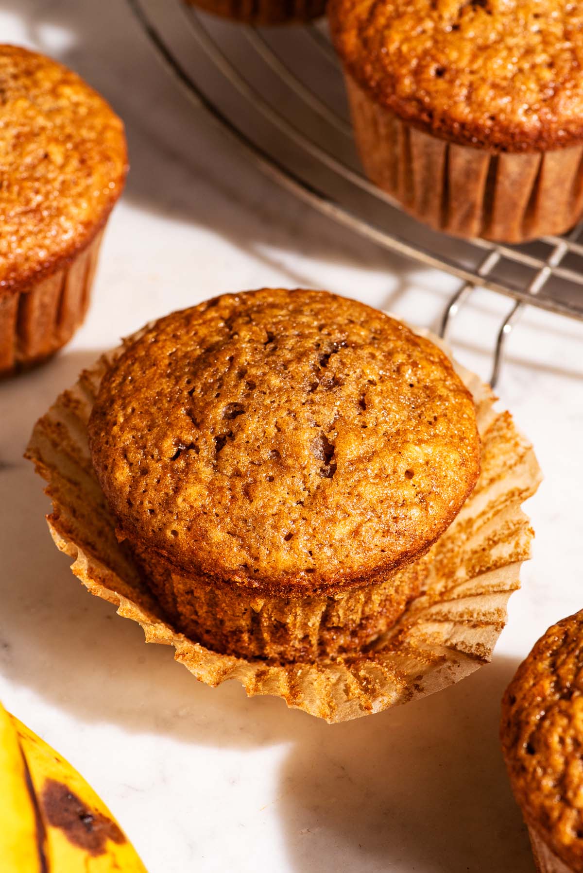 Four muffins on a marble counter, one with the paper lining removed.