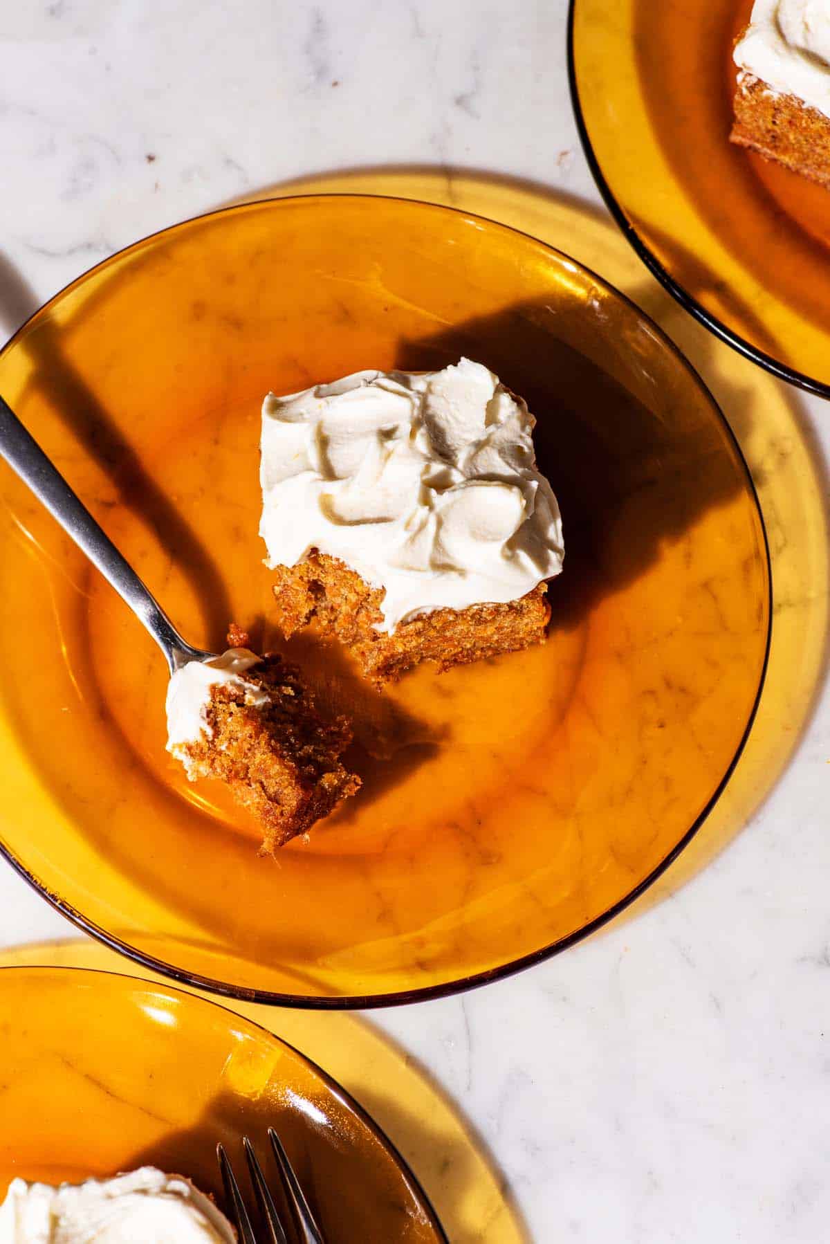 Pieces of frosted carrot cake on orange glass plates.